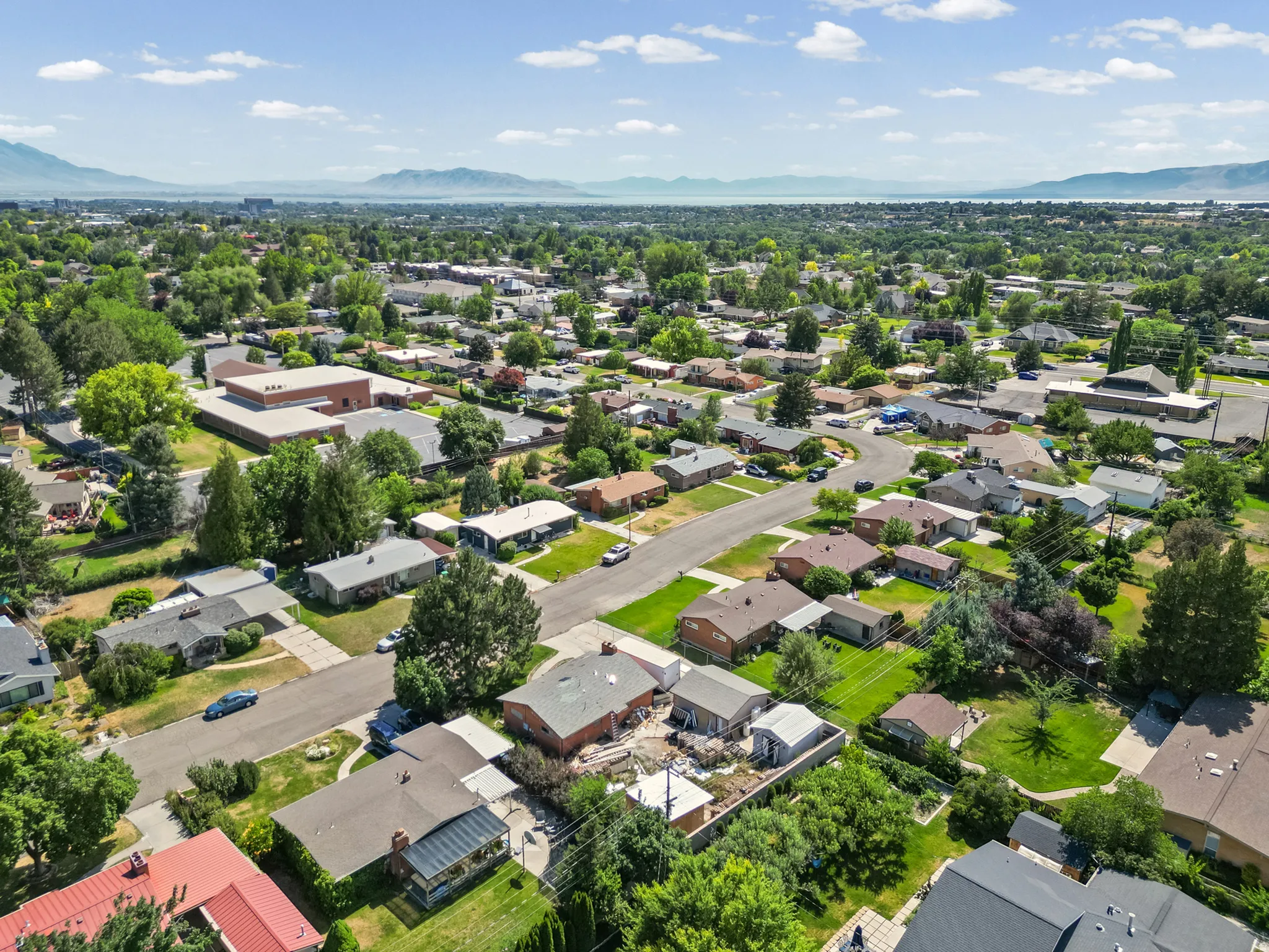 Expansive aerial perspective showcasing a residential area with mature tree coverage, mountain backdrop, and distant body of water