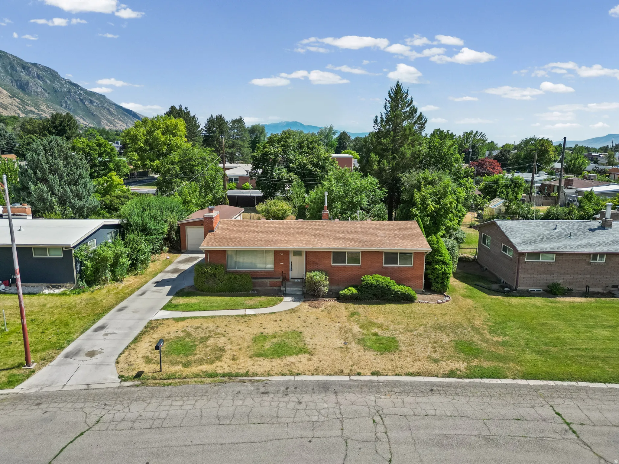 Red brick residence featuring a brown shingle roof, attached garage, front yard with mature landscaping, and a concrete driveway