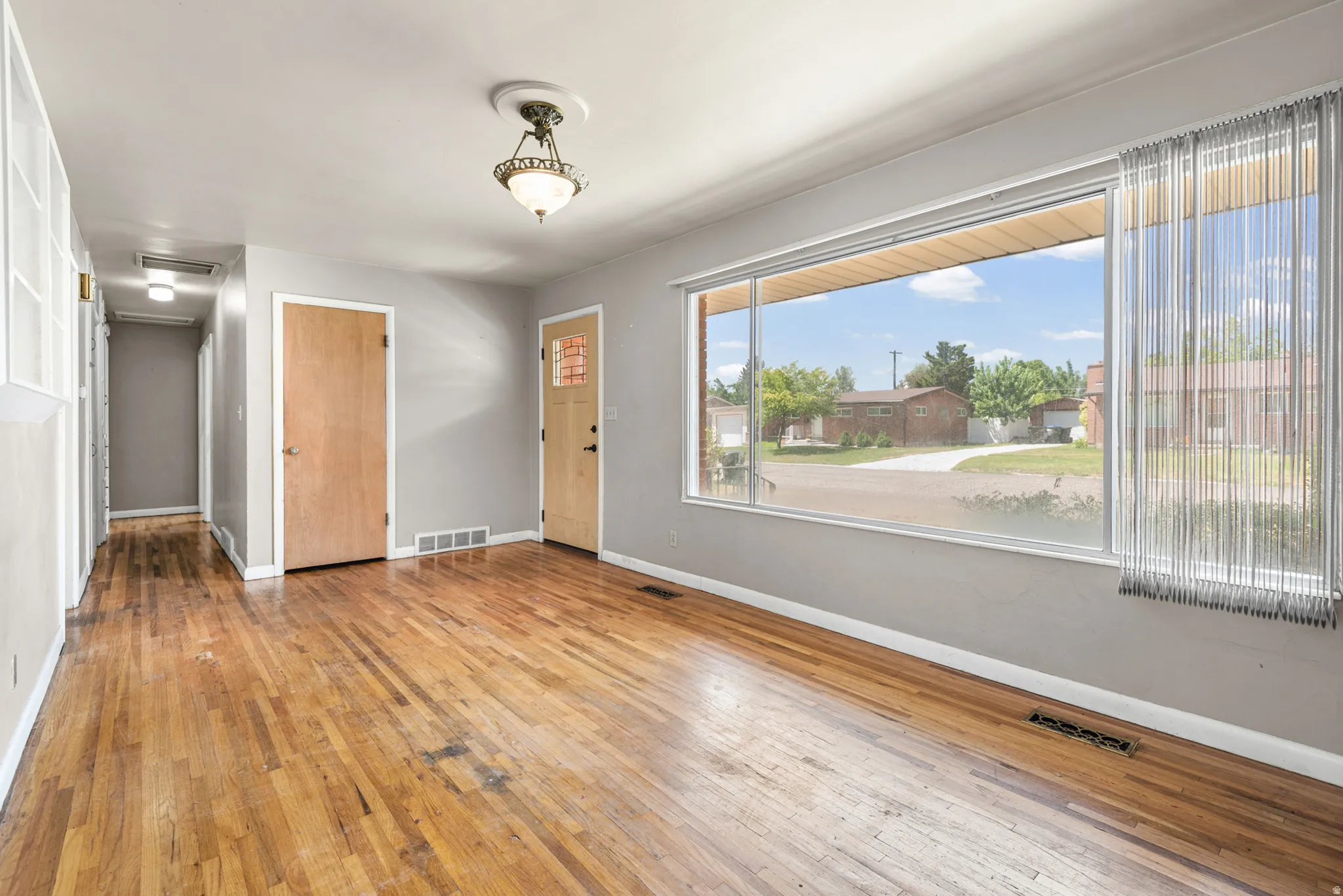 Hardwood flooring throughout, featuring a large picture window, light gray wall tones, and recessed ceiling lighting