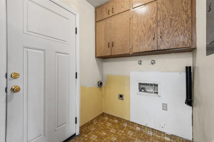 Utility space featuring wood-finish cabinetry, a white paneled door with brass hardware, and patterned floor tile