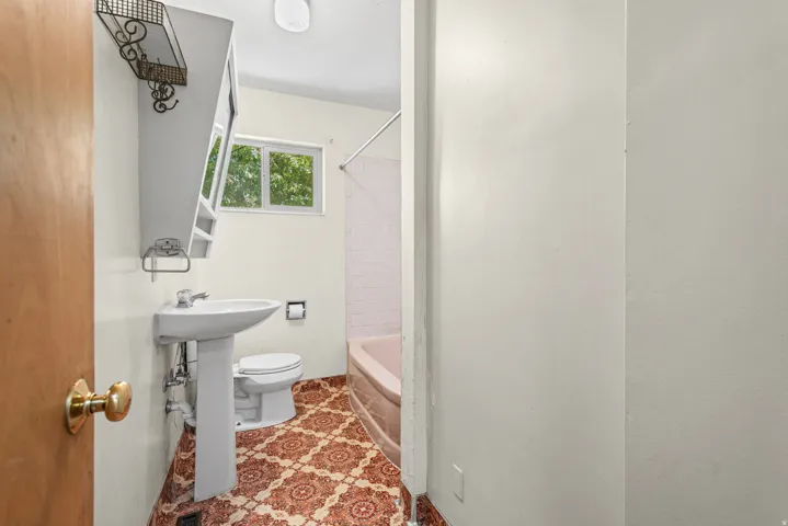 Bathroom featuring a pedestal sink, patterned floor tiling, and a window