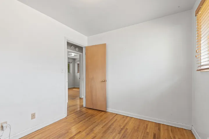 Room with wood-finish flooring, a light wood door, and a window with wood blinds