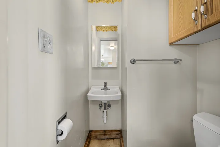 Compact powder room featuring a wall-mounted sink with chrome faucet, a recessed toilet paper holder, and a wood-finish floor