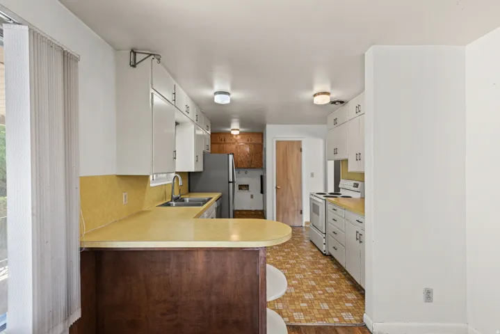 Kitchen featuring ample white cabinetry, a double basin stainless steel sink, a built-in breakfast bar with a wood-finish base, and integrated ceiling lighting