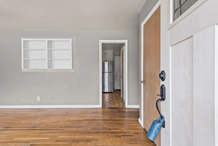 Entryway featuring a white paneled door with black hardware, wood-finish flooring, light gray walls, and a recessed built-in shelving unit