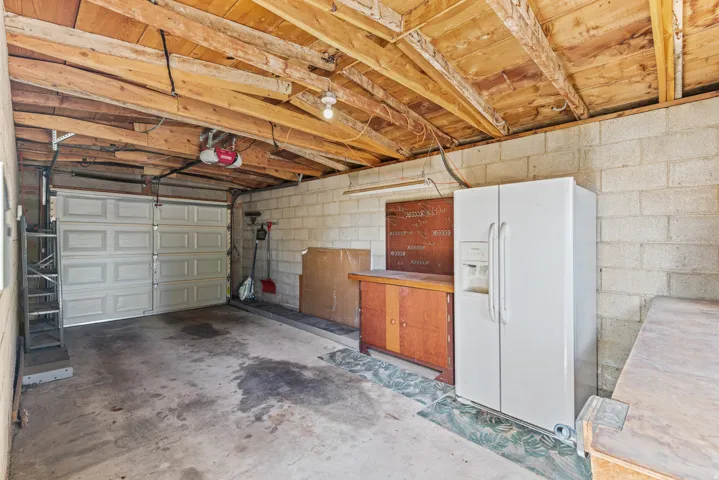 Single-bay garage with concrete block walls, exposed wood beam ceiling, and a paneled garage door