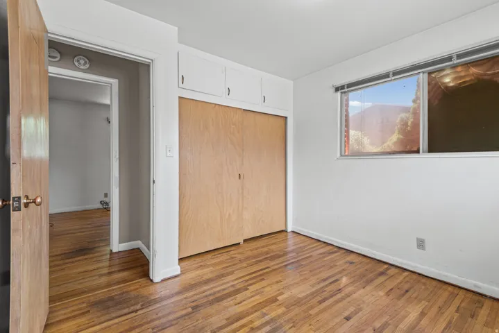 Hardwood flooring throughout, featuring a built-in closet with natural wood doors and overhead cabinetry