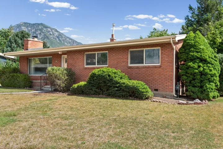 Brick exterior featuring a front porch with railing, mature landscaping, and a mountainous backdrop