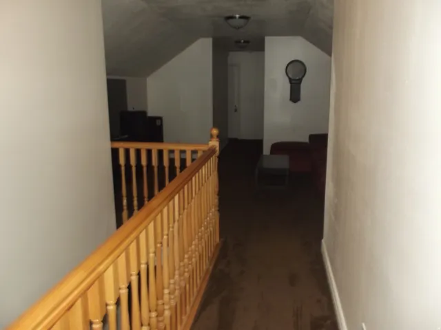 Wood-finish banister alongside a carpeted hallway with sloped ceilings and recessed lighting