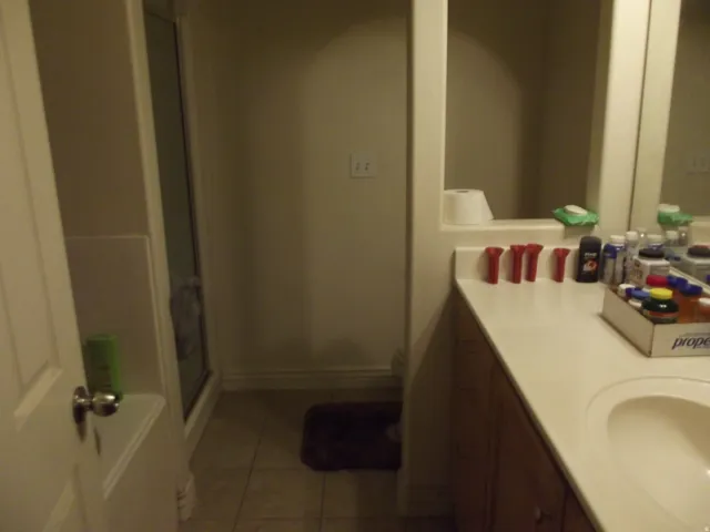 Bathroom featuring a dual-sink vanity with light-colored countertops, wood-finish cabinetry, a built-in mirror, and tiled flooring