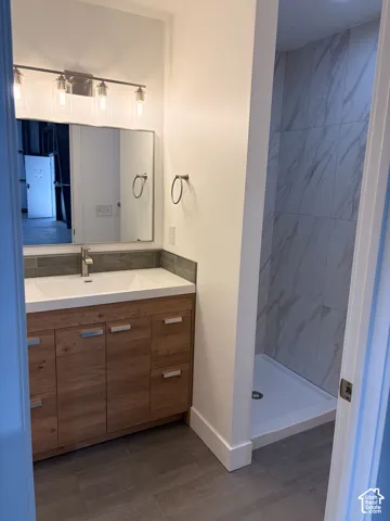 Bathroom featuring a wood-finish vanity with a built-in sink, a tiled backsplash, and a framed mirror