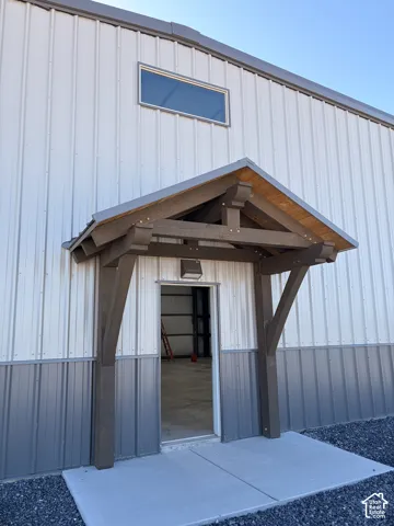 Front entry featuring a timber-frame awning, metal siding, concrete pad, and gravel surround