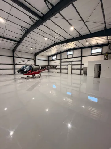 Spacious hangar featuring a high ceiling with exposed steel beams, multiple windows, and a polished concrete floor