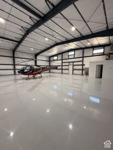 Spacious hangar featuring a high ceiling with exposed steel beams, multiple windows, and a polished concrete floor
