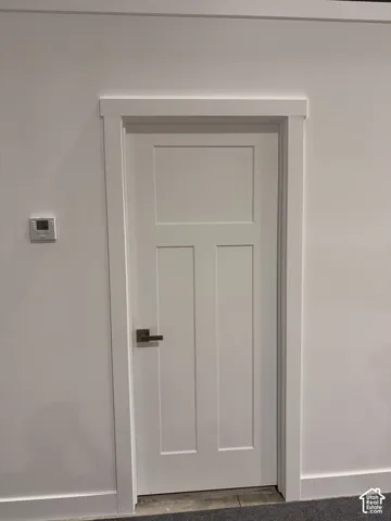 White paneled door with a bronze lever handle, framed by white trim and baseboards