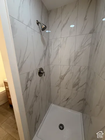 Shower enclosure featuring large format white and gray veined wall tiles, a white shower pan, and a brushed nickel shower head with coordinating controls