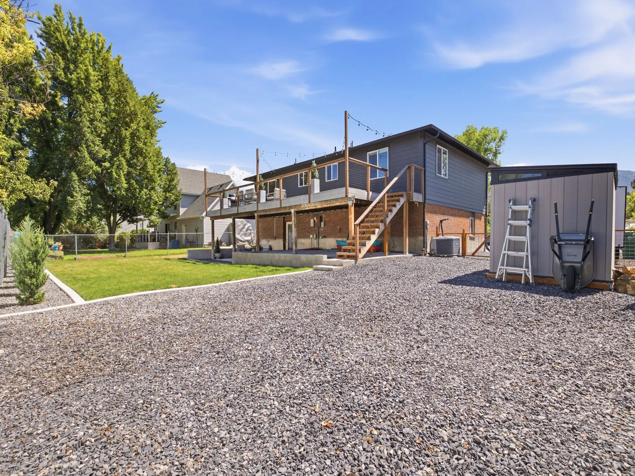 Rear exterior featuring a spacious gravel driveway, an upper-level deck with wood railing, and a ground-level patio area