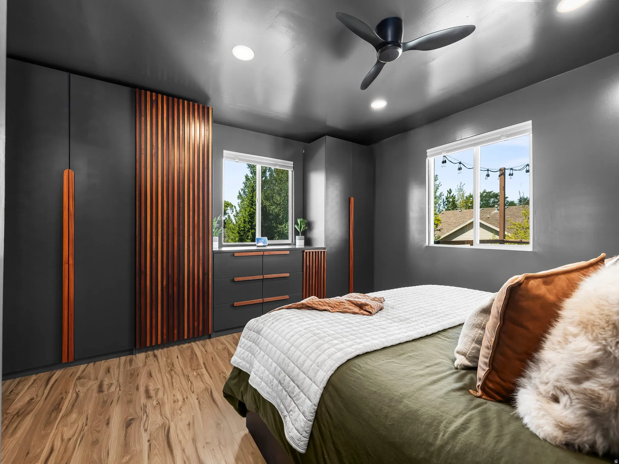 Modern bedroom featuring wood-finish flooring and two large windows