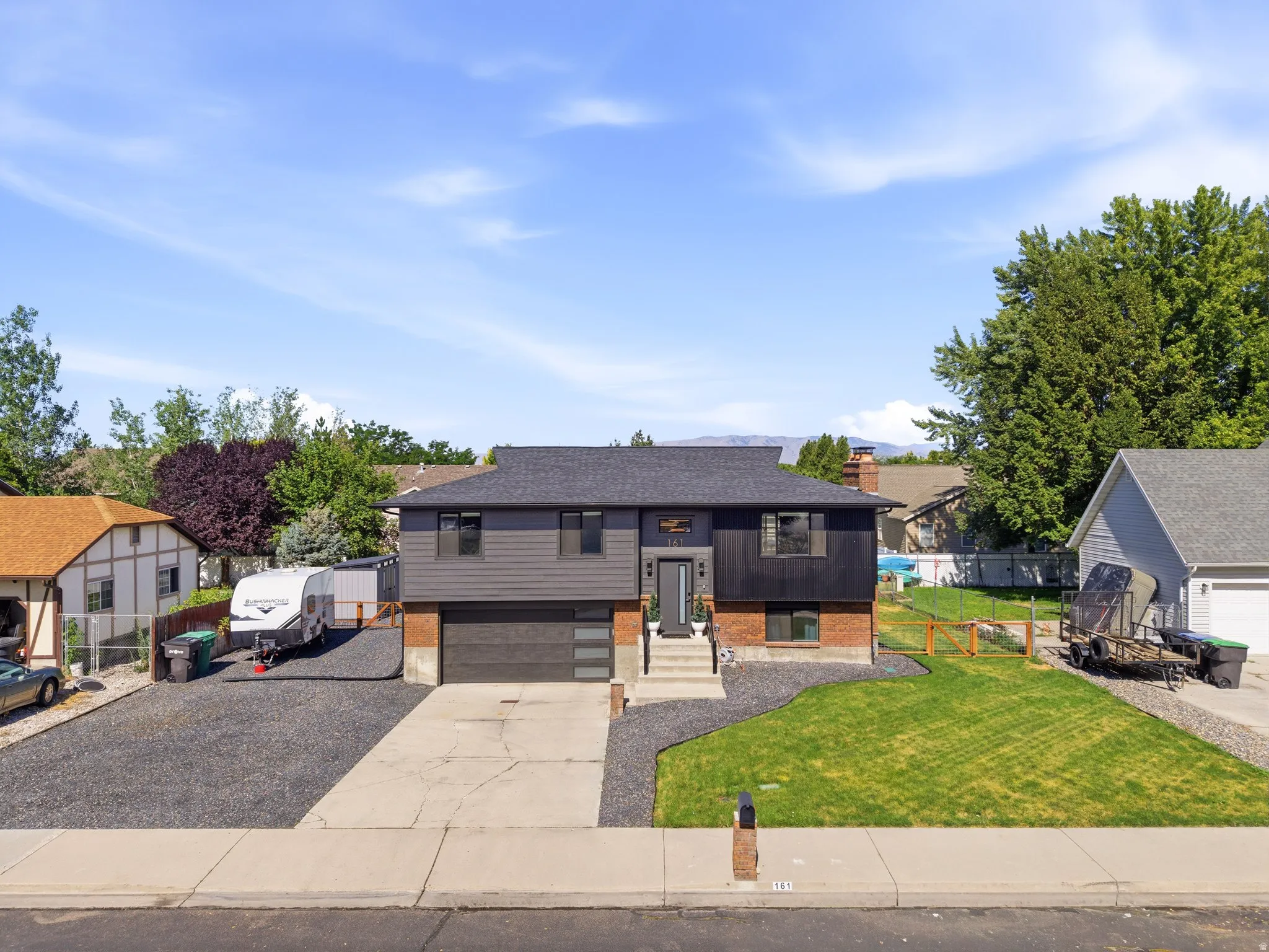 Split-level residence featuring a dark gray and black exterior with brick accents