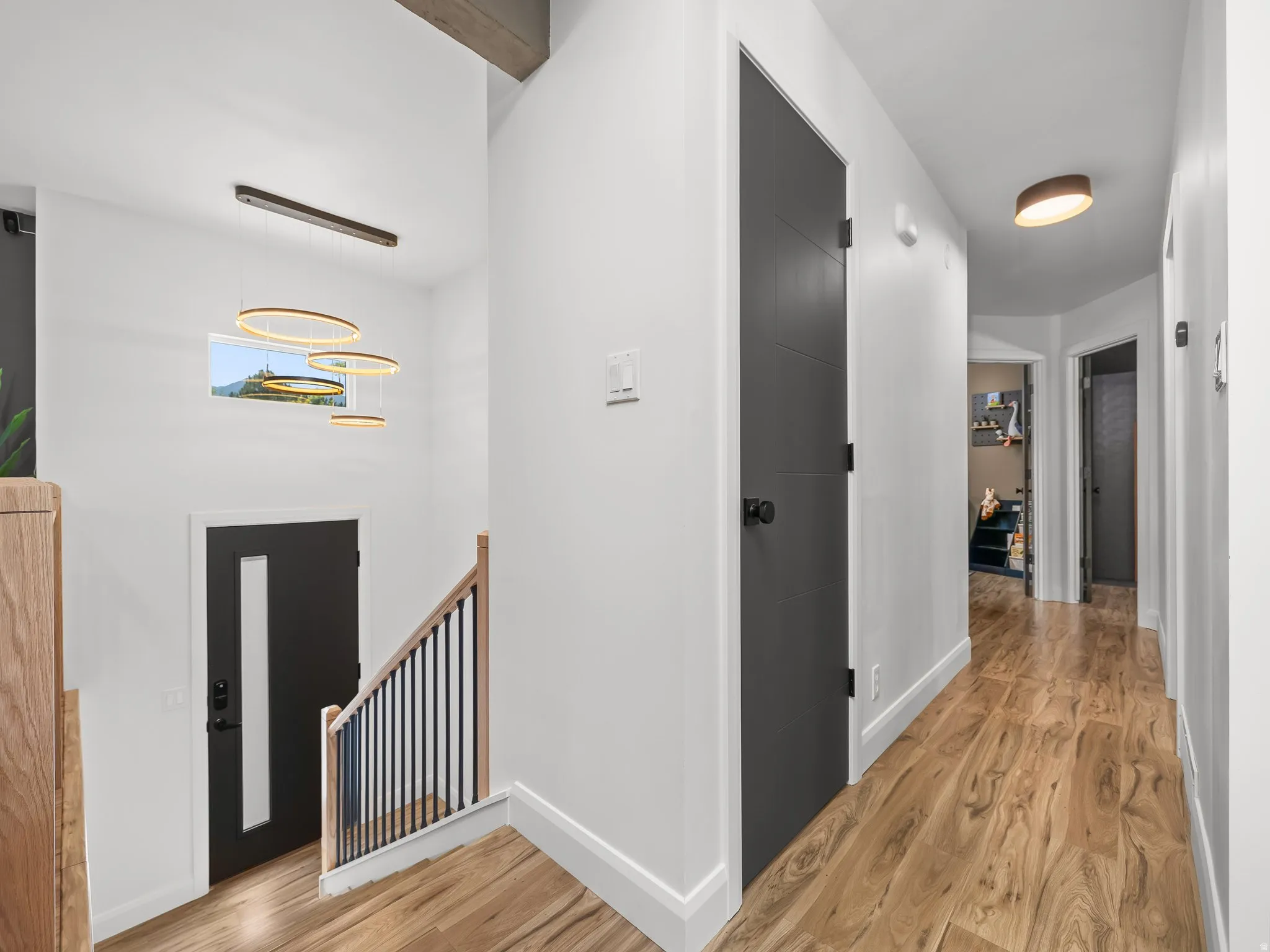 Bright interior hallway featuring wood-finish flooring, white walls, and contemporary light fixtures