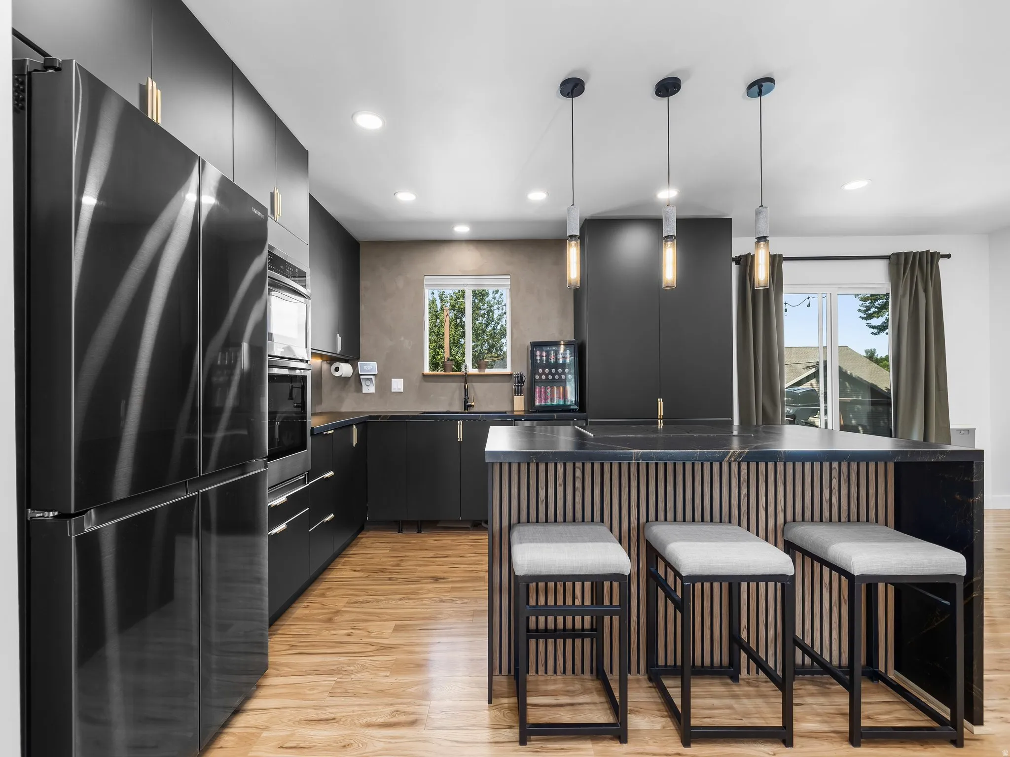 Modern kitchen featuring sleek black cabinetry, integrated black stainless steel appliances, and wood-finish flooring
