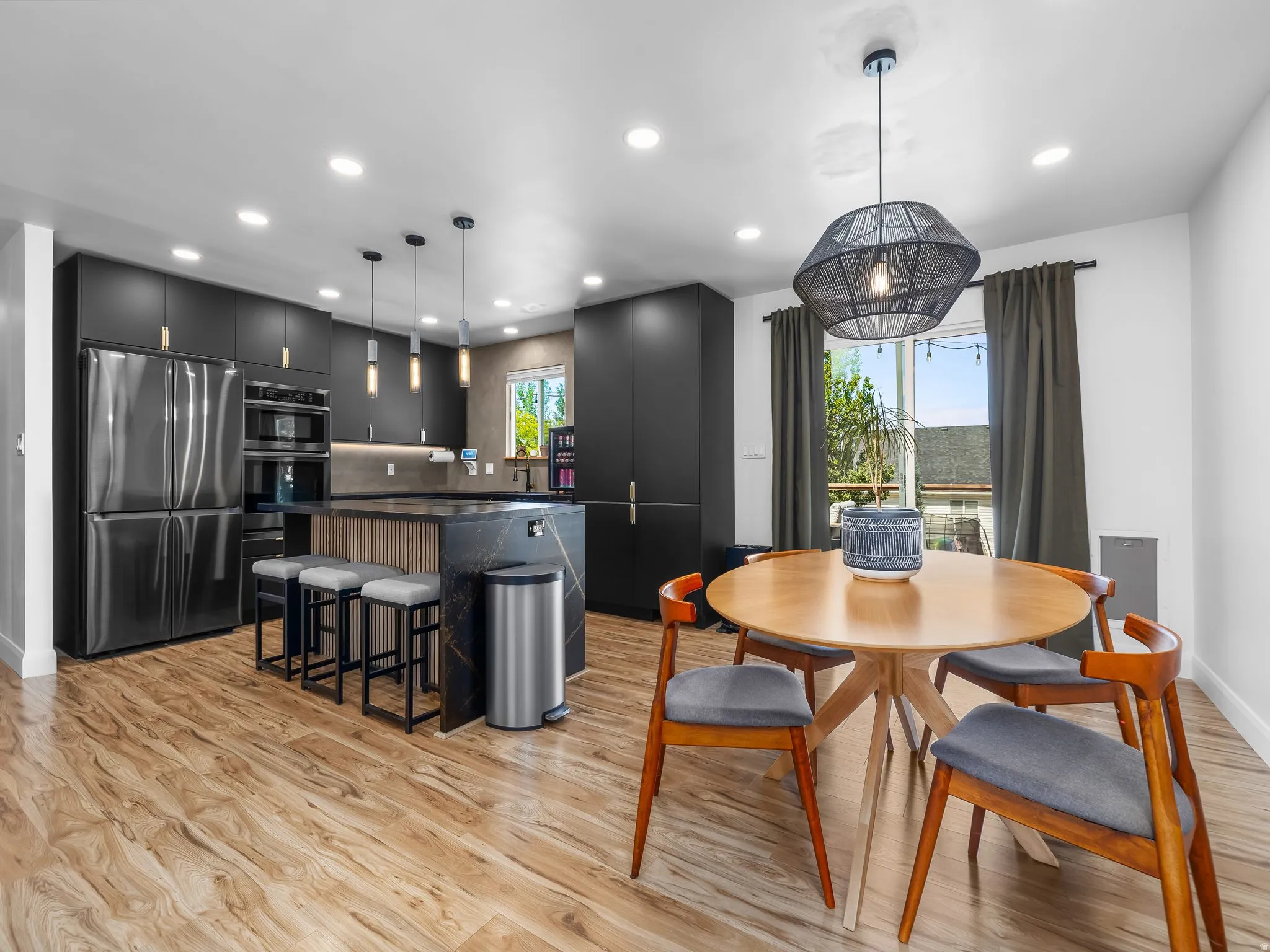 Contemporary kitchen featuring sleek black cabinetry, stainless steel appliances, and a waterfall island with stone countertop