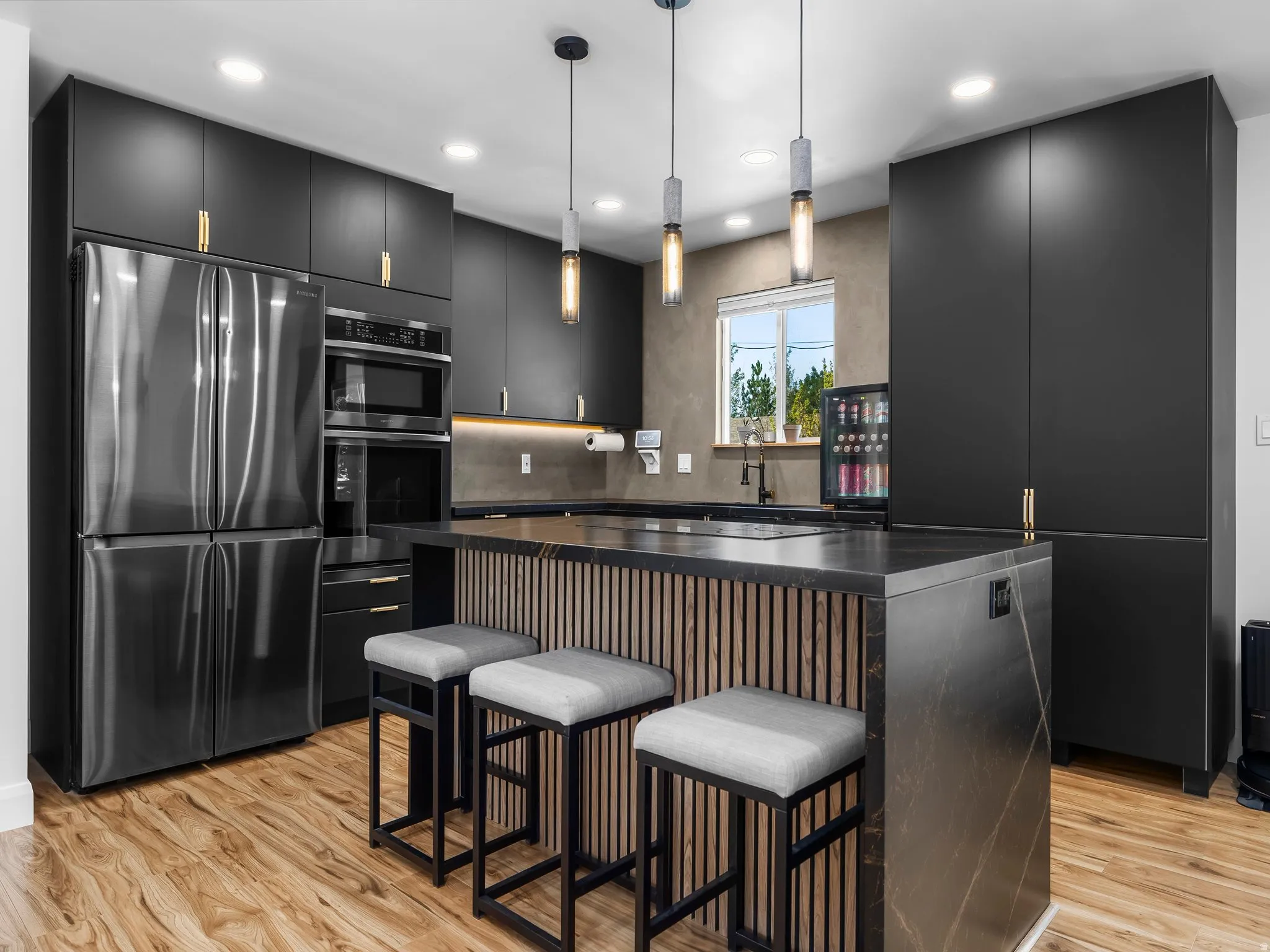 Contemporary kitchen featuring matte black cabinetry with gold-tone hardware, a dark-toned refrigerator, and built-in double ovens
