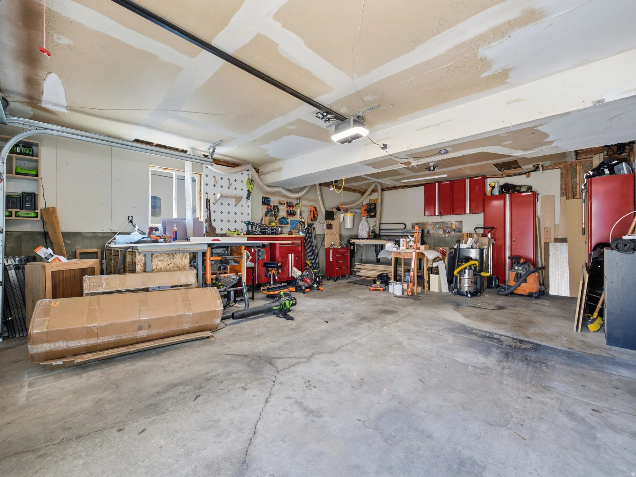 Spacious garage featuring a concrete floor, overhead garage door with opener, recessed lighting, a window, and built-in red cabinetry