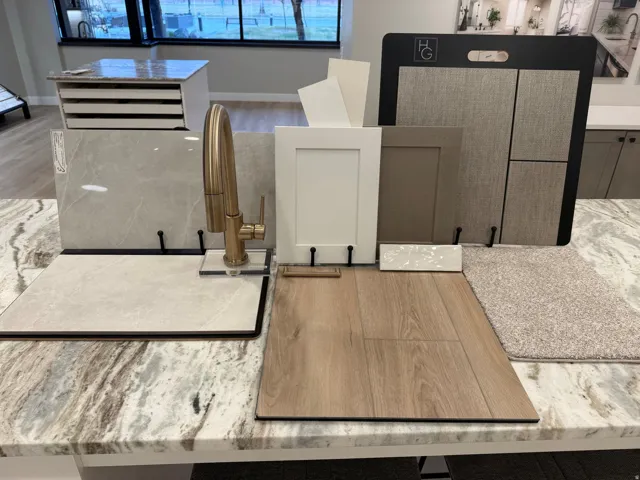Curated selection of interior finishes featuring a gold-toned faucet, white shaker cabinet door, light wood-finish flooring, and a patterned stone countertop