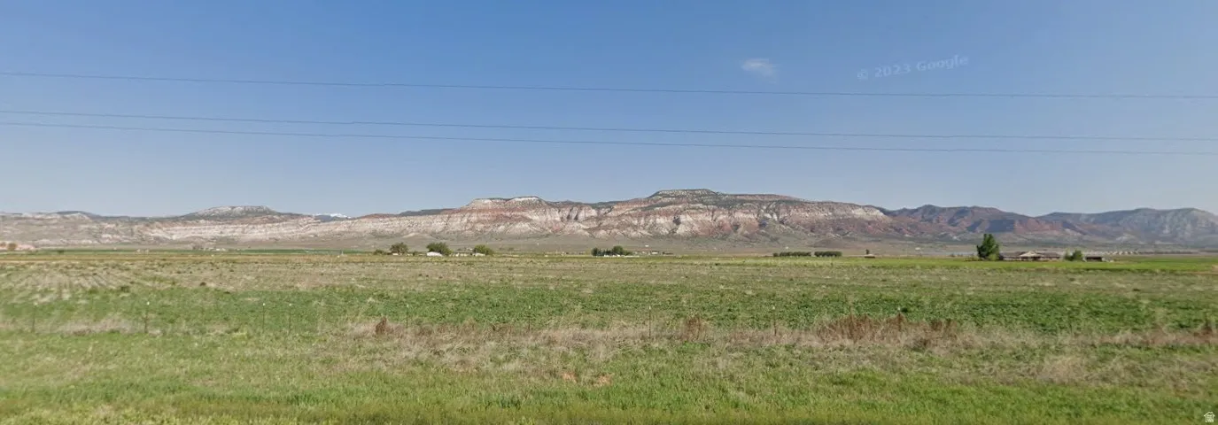 Expansive open fields featuring green and dry vegetation, bordered by distant mountainous terrain with visible rock formations