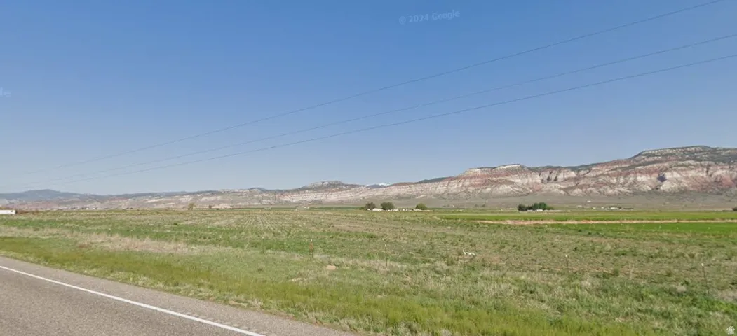 Expansive land featuring a paved road, green fields, and distant mountains under a clear sky