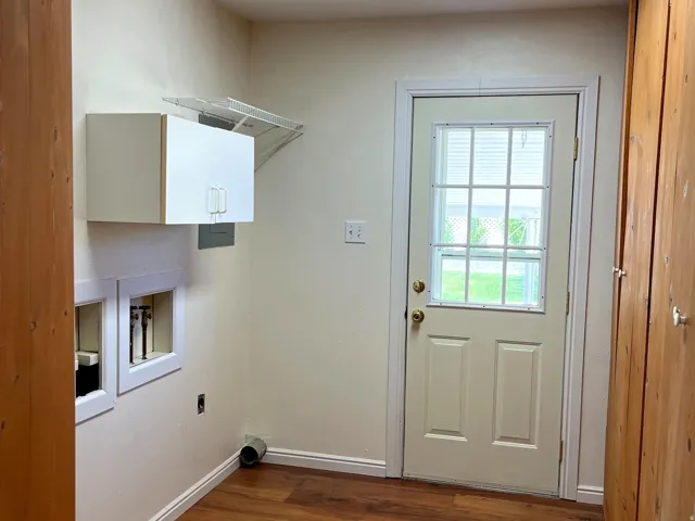 Functional utility room featuring wood-finish flooring, a paneled door with an integrated window, wall-mounted cabinetry, and dedicated laundry hookups