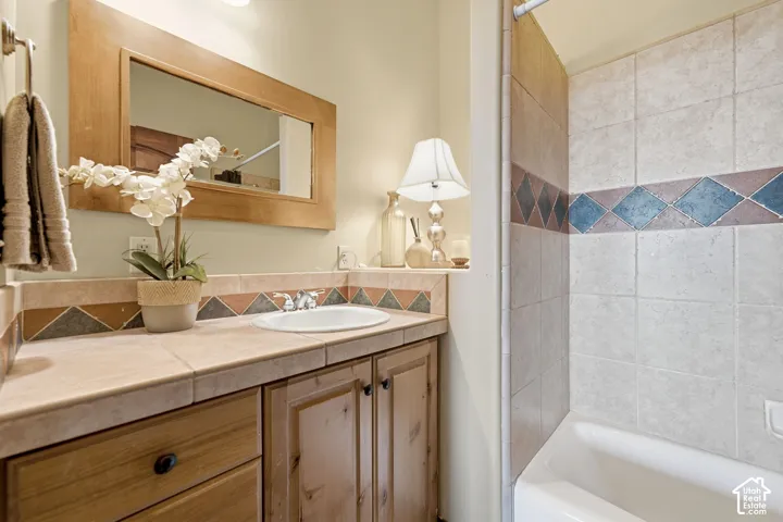Bathroom vanity with wood-finish cabinetry, tile countertop, and an integrated basin sink
