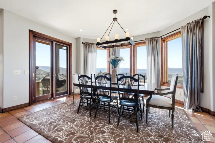 Dining area featuring multiple large windows, wood-framed glass doors, a rectangular chandelier, recessed lighting, and terracotta tile flooring