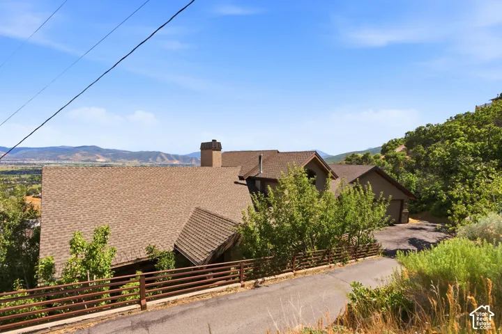 Property situated on a sloped landscape, featuring a multi-level roofline with asphalt shingles and a prominent chimney structure
