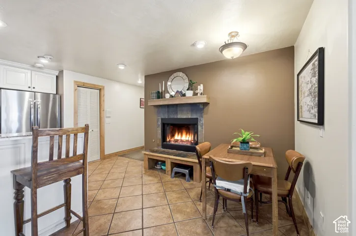 Open-concept area featuring a stone-clad fireplace with a wood mantel, tile flooring, and white cabinetry with stainless steel appliances