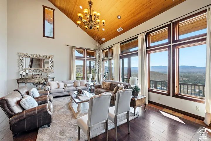 Expansive living area featuring a vaulted wood-finish ceiling, dark wood-finish flooring, a large chandelier, and a wall of windows showcasing distant landscapes