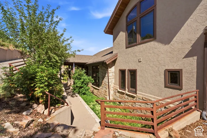 Stucco and stone exterior featuring varied window styles, a gabled roofline, and a concrete pathway with metal handrails