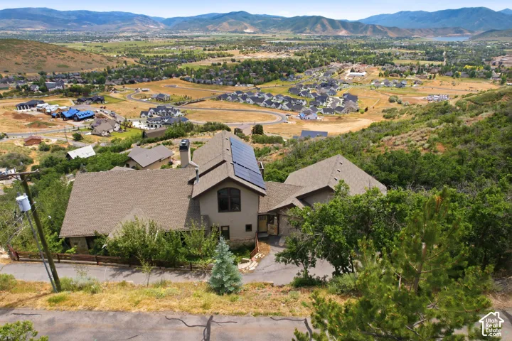 Expansive mountain and valley scenery featuring a residential property with a multi-gabled roofline, solar panels, and mature landscaping
