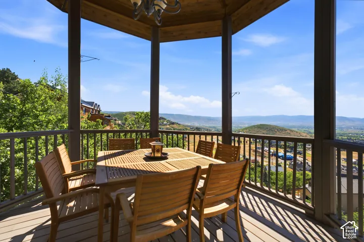 Covered outdoor deck with wood-finish flooring, featuring a slatted railing and overhead chandelier