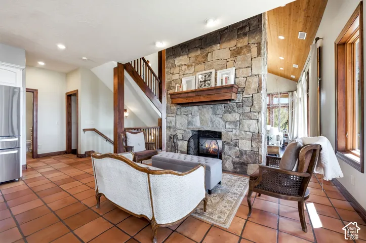 Living area featuring a stone fireplace with a wood mantle, terracotta tile flooring, and vaulted wood-paneled ceilings