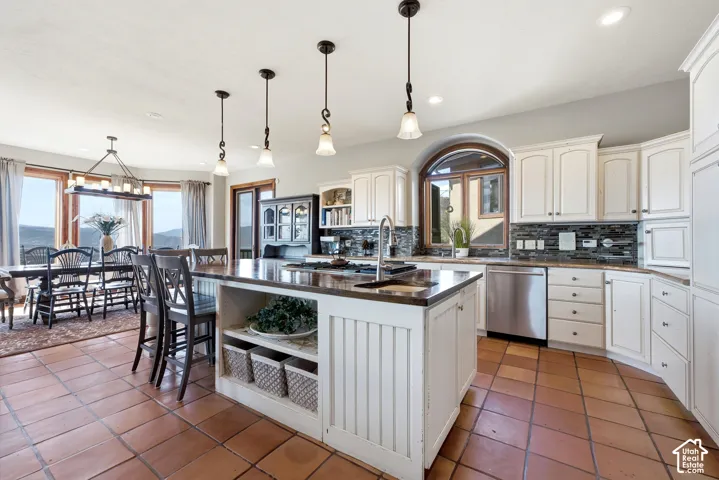 Open-concept kitchen and dining area featuring terra cotta tile flooring, white cabinetry, a large kitchen island with seating, a mosaic tile backsplash, and stainless steel appliances
