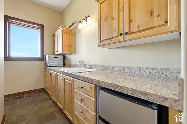 Utility area featuring light wood cabinetry with dark hardware, a single basin sink, and a built-in compact refrigerator