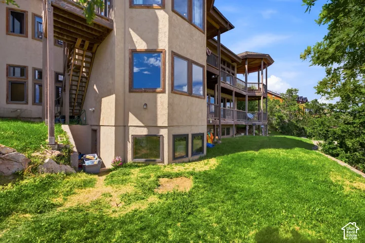 Multi-level exterior featuring stucco siding, multiple balconies with wood railings, a dedicated porch area, and an expansive grassy slope