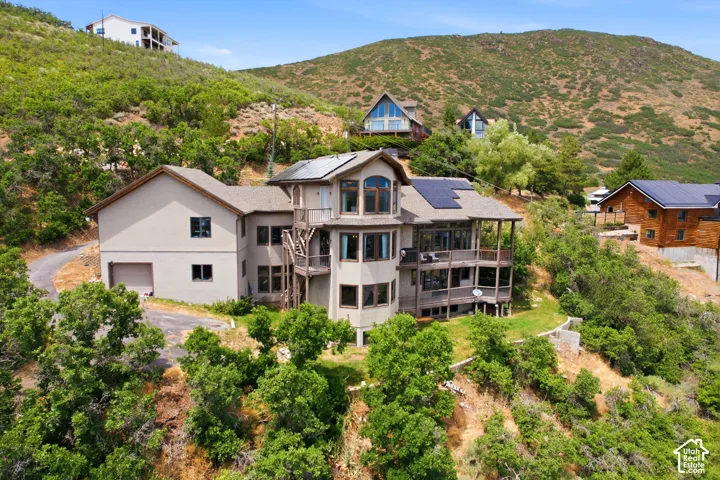Multi-level hillside residence featuring a tan exterior, dark trim windows, and solar panels on a brown shingle roof