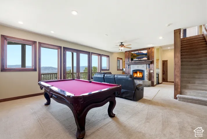 Lower-level recreation space featuring a stone fireplace with wood surround, multiple windows, double French doors, and carpeted flooring