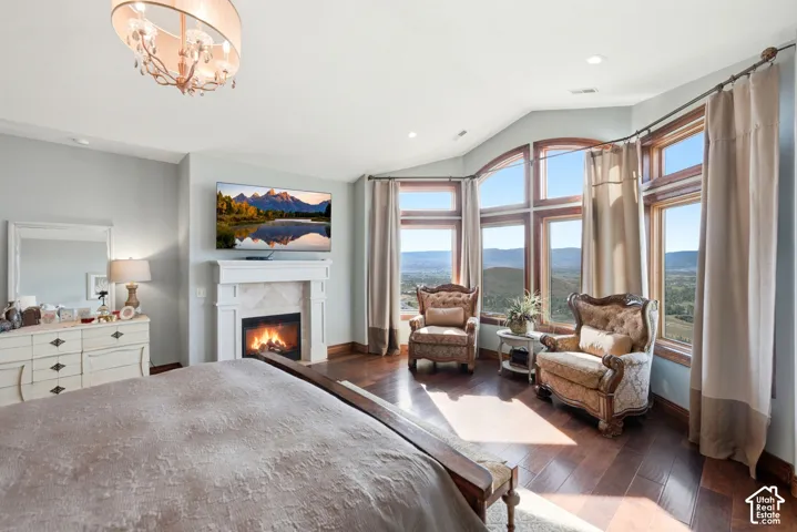 Hardwood flooring throughout this room featuring a fireplace with a white mantel, an ornate chandelier, and a large bay window with arched detailing
