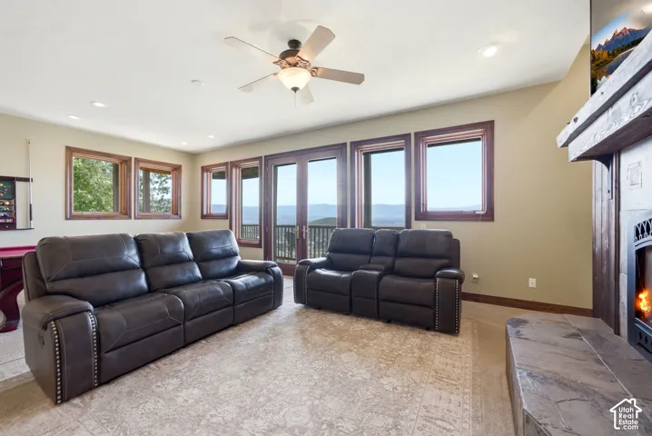 Spacious room featuring multiple windows and glass doors with mountain scenery, a built-in stone fireplace with wood mantel, recessed lighting, and a ceiling fan