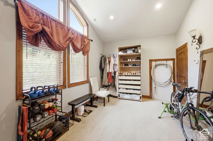 Vaulted ceiling room featuring natural wood-framed windows, recessed lighting, a built-in storage unit with open shelving and drawers, a wood-paneled door, and neutral-toned wall paint