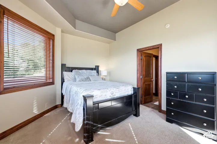 Carpeted bedroom featuring a large window with wood-finish blinds, a ceiling fan, and wood-trim door frames